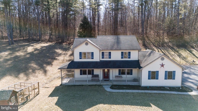 view of front facade featuring roof with shingles, covered porch, and a front yard