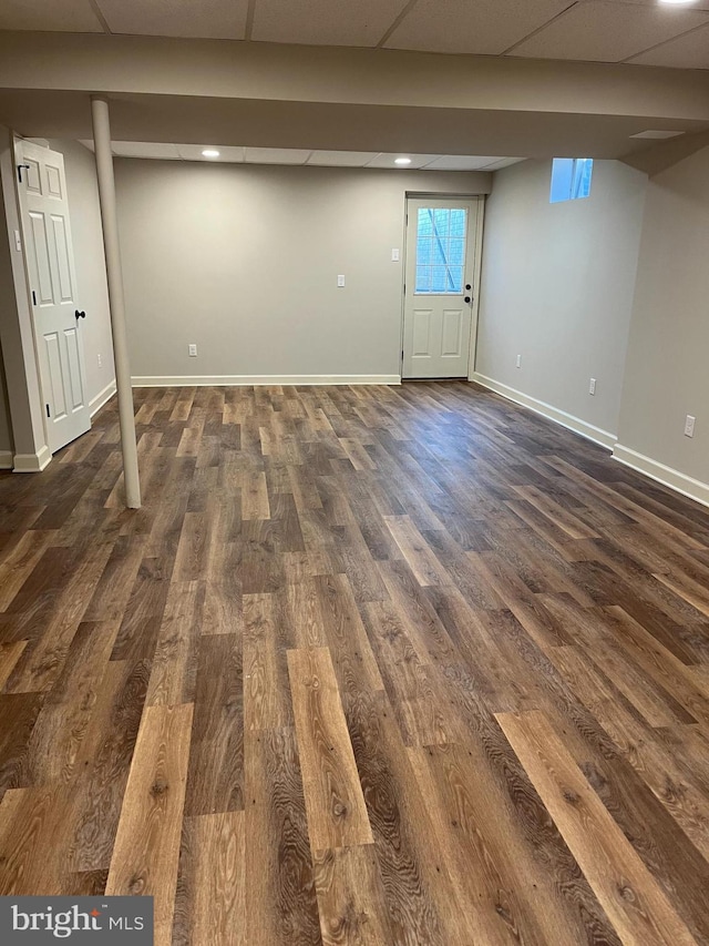 below grade area with baseboards, dark wood-style flooring, and a drop ceiling