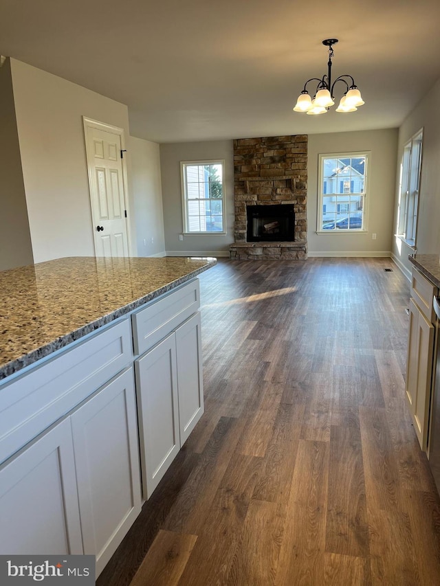 kitchen with decorative light fixtures, light stone counters, a fireplace, white cabinets, and dark wood-style flooring