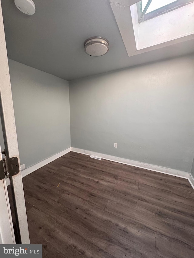 spare room with baseboards, a skylight, and dark wood-style flooring