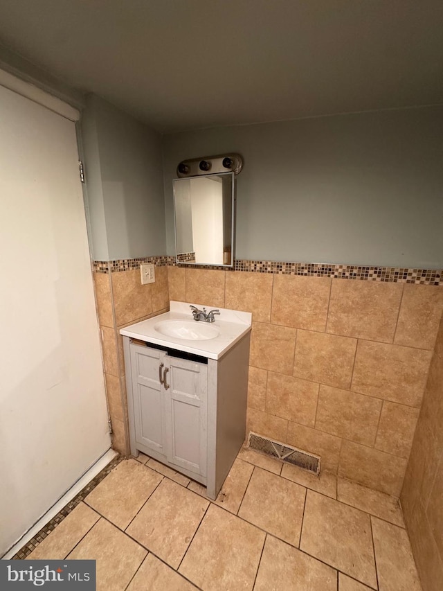 bathroom featuring vanity, visible vents, wainscoting, tile patterned floors, and tile walls