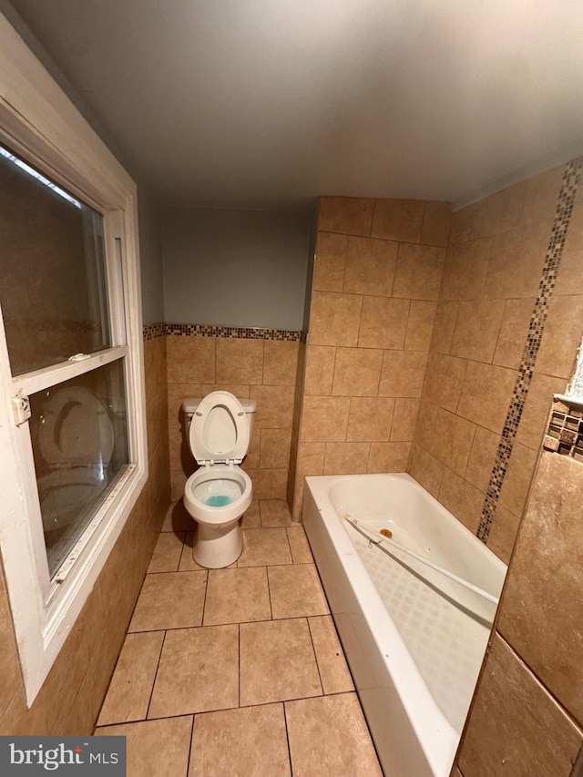 bathroom featuring tile patterned floors, toilet, tile walls, and a tub to relax in