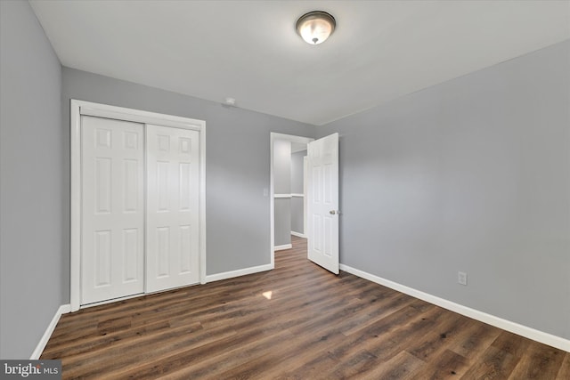 unfurnished bedroom with dark wood finished floors, a closet, and baseboards