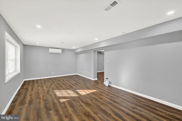 below grade area with baseboards, visible vents, recessed lighting, an AC wall unit, and dark wood-type flooring