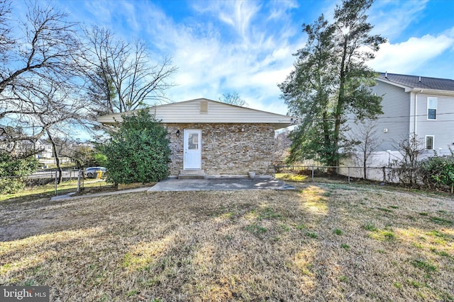 rear view of property featuring a yard, stone siding, a patio, and fence