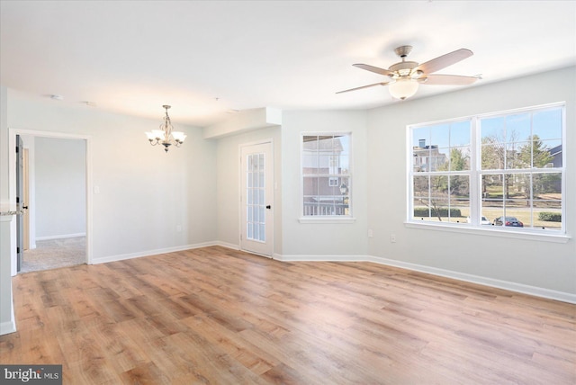 empty room with ceiling fan with notable chandelier, baseboards, and light wood finished floors