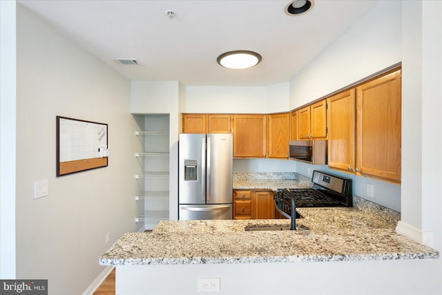 kitchen featuring light stone counters, a sink, stainless steel appliances, a peninsula, and brown cabinetry