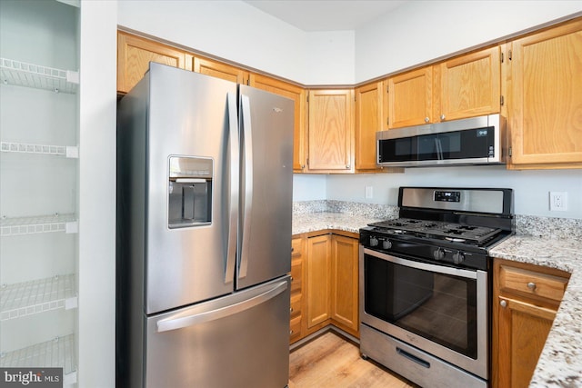 kitchen with light stone counters, light wood finished floors, and stainless steel appliances