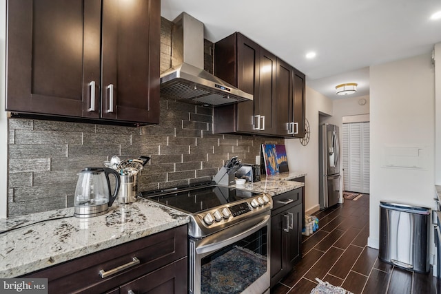 kitchen with light stone countertops, wood tiled floor, stainless steel appliances, dark brown cabinetry, and wall chimney exhaust hood