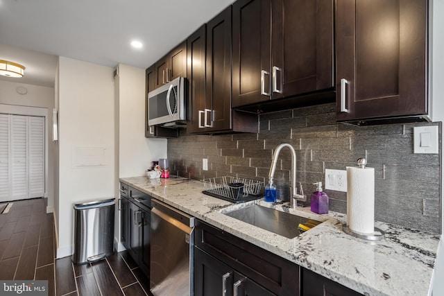 kitchen with a sink, light stone counters, appliances with stainless steel finishes, dark brown cabinets, and wood tiled floor