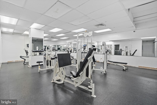 workout area with visible vents, a paneled ceiling, and baseboards