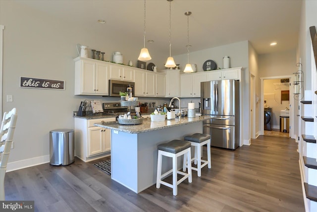 kitchen with light stone countertops, washer / dryer, appliances with stainless steel finishes, dark wood-style floors, and white cabinets