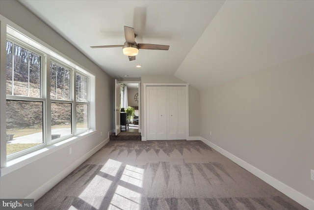 unfurnished bedroom featuring baseboards, light colored carpet, vaulted ceiling, a closet, and a ceiling fan