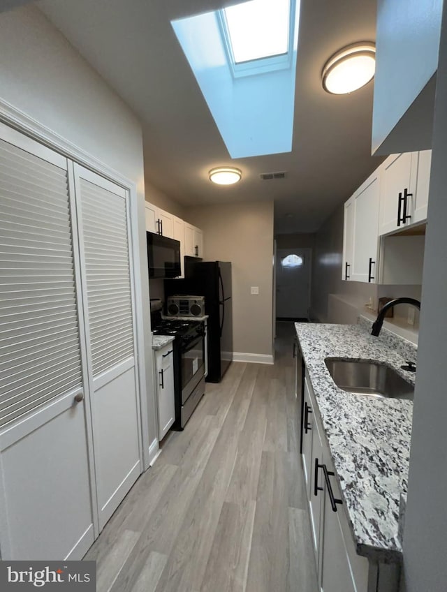 kitchen featuring visible vents, black appliances, a sink, a skylight, and white cabinets