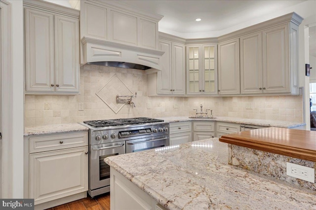 kitchen with decorative backsplash, glass insert cabinets, light stone counters, and double oven range