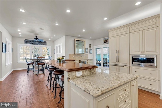 kitchen with stainless steel microwave, light stone countertops, cream cabinetry, and light wood finished floors