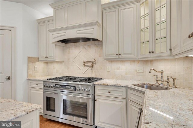 kitchen featuring backsplash, double oven range, light stone countertops, and a sink