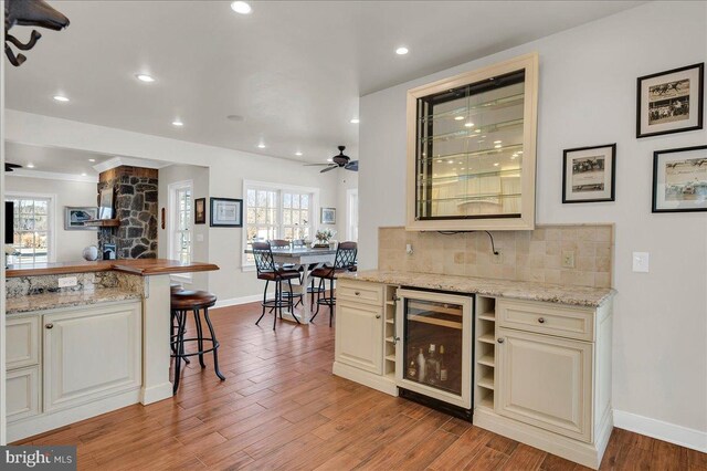 kitchen with wood finished floors, light stone countertops, beverage cooler, a kitchen bar, and backsplash