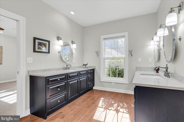 bathroom featuring a sink, baseboards, two vanities, and wood finished floors