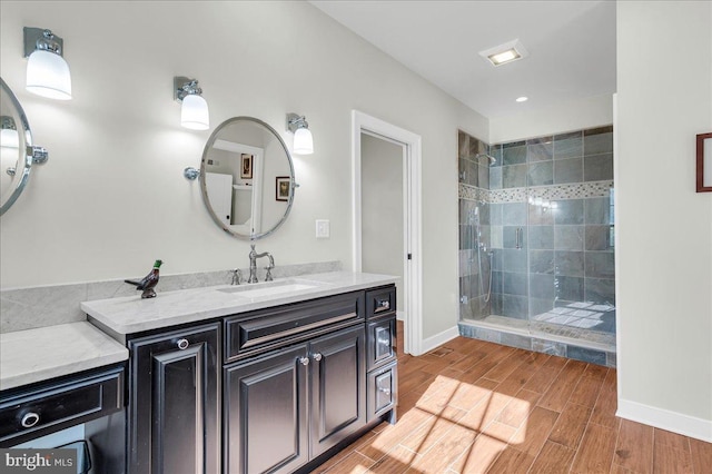 bathroom with wood finish floors, baseboards, vanity, and a tile shower