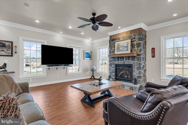 living room with a stone fireplace, crown molding, baseboards, and wood finished floors