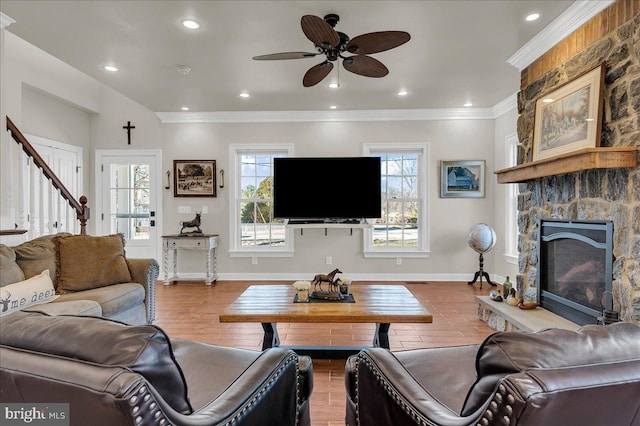 living area with wood finished floors, baseboards, recessed lighting, a stone fireplace, and crown molding