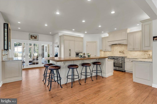 kitchen with french doors, light wood finished floors, backsplash, and stainless steel range