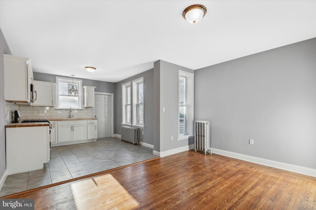 kitchen featuring a sink, backsplash, stainless steel range with gas stovetop, and radiator heating unit