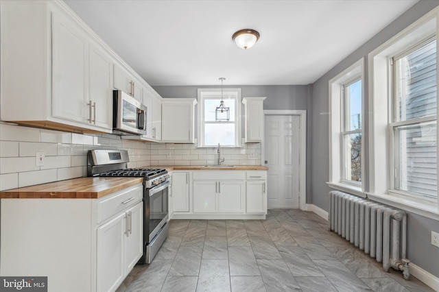 kitchen featuring radiator, a sink, stainless steel appliances, wood counters, and white cabinetry