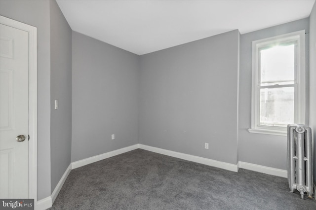 spare room with radiator heating unit, baseboards, and dark colored carpet