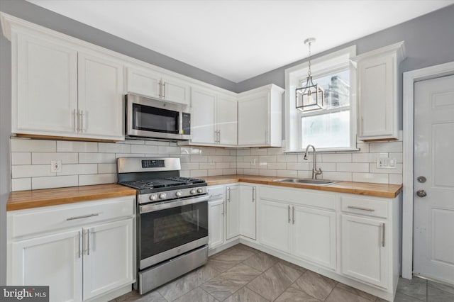 kitchen with wooden counters, appliances with stainless steel finishes, white cabinetry, and a sink