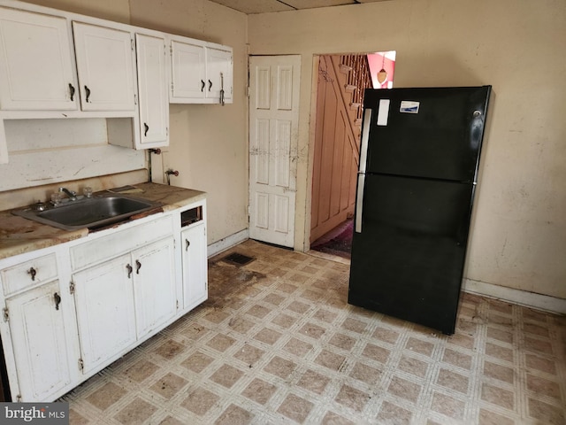 kitchen featuring a sink, white cabinetry, freestanding refrigerator, baseboards, and light floors