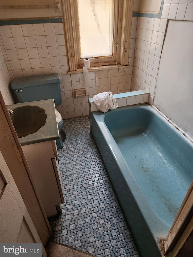 bathroom with tile patterned flooring, tile walls, toilet, a tub to relax in, and vanity