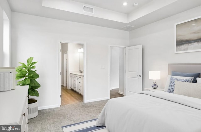 bedroom with visible vents, connected bathroom, baseboards, light colored carpet, and a tray ceiling