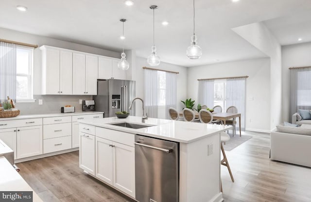 kitchen with open floor plan, a center island with sink, light wood-type flooring, appliances with stainless steel finishes, and a sink