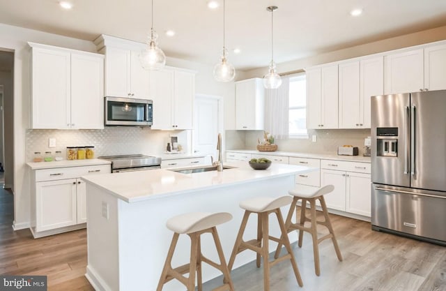 kitchen with a center island with sink, light wood-style flooring, a sink, decorative backsplash, and stainless steel appliances