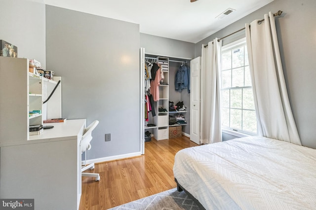 bedroom featuring a spacious closet, visible vents, baseboards, wood finished floors, and a closet