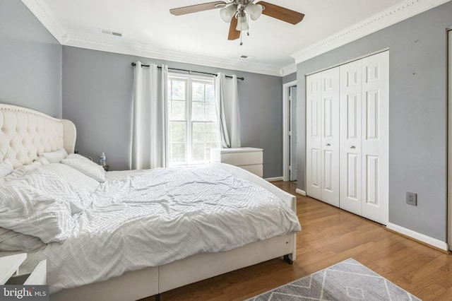 bedroom featuring wood finished floors, visible vents, baseboards, a closet, and crown molding