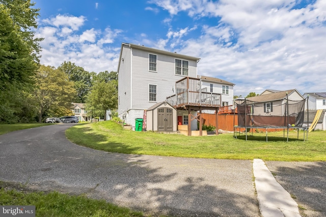 back of property featuring an outbuilding, a wooden deck, a yard, a storage unit, and a trampoline