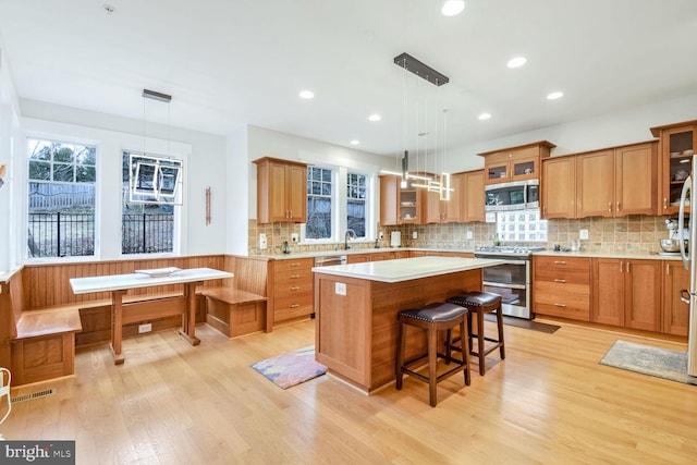 kitchen with visible vents, a kitchen island, glass insert cabinets, light wood-style flooring, and stainless steel appliances