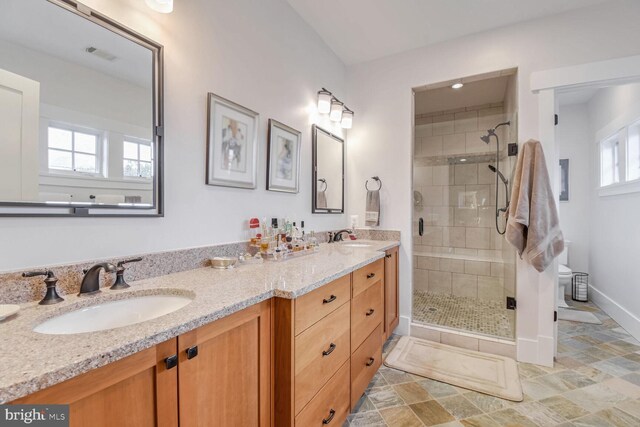 full bath with baseboards, toilet, double vanity, a stall shower, and a sink