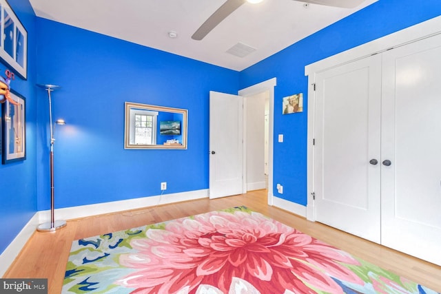 bedroom with visible vents, wood finished floors, a closet, baseboards, and ceiling fan