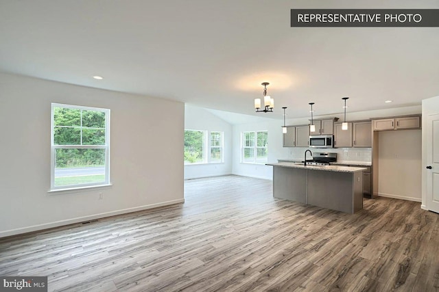 kitchen featuring wood finished floors, baseboards, an inviting chandelier, stainless steel appliances, and open floor plan