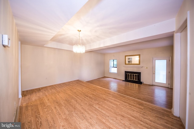 24 W Orange Ct, Baltimore, MD 21234 - unfurnished living room featuring a chandelier, wood finished floors, a glass covered fireplace, baseboards, and a tray ceiling
