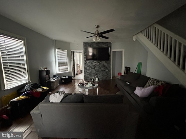 living room with stairs, a stone fireplace, wood finished floors, and a ceiling fan