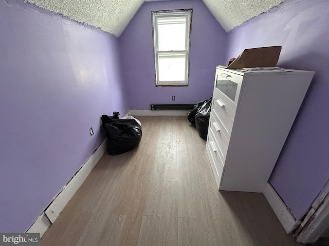 additional living space with light wood-type flooring, lofted ceiling, and a textured ceiling