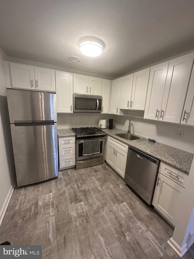 kitchen with light stone countertops, a sink, stainless steel appliances, dark wood-type flooring, and white cabinetry