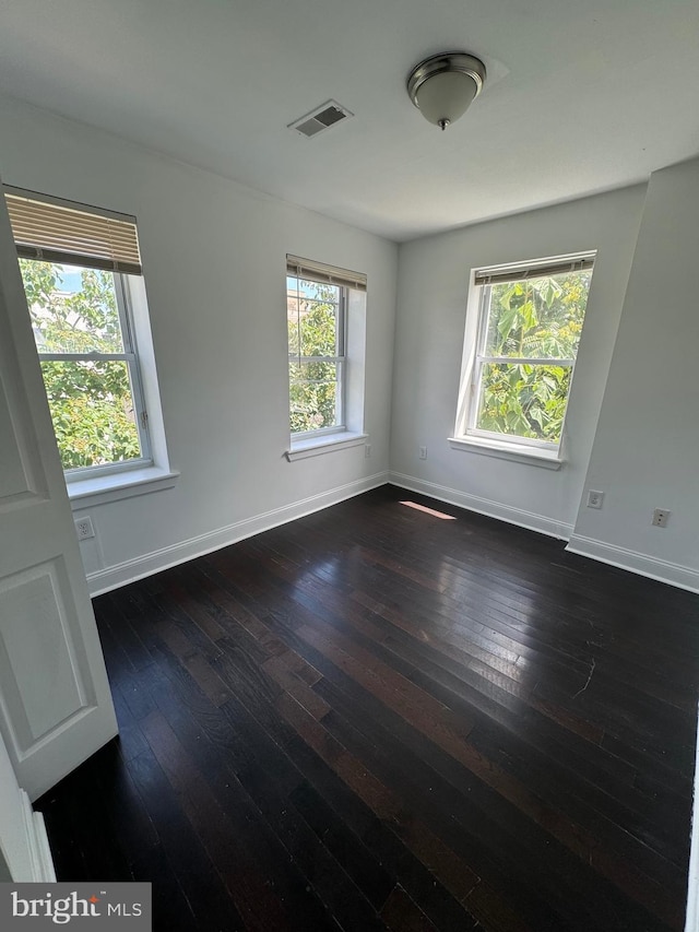 spare room featuring visible vents, dark wood-type flooring, and baseboards