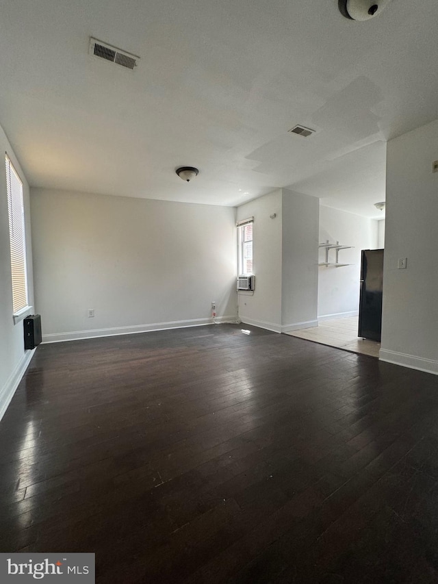 unfurnished room featuring dark wood finished floors, cooling unit, baseboards, and visible vents