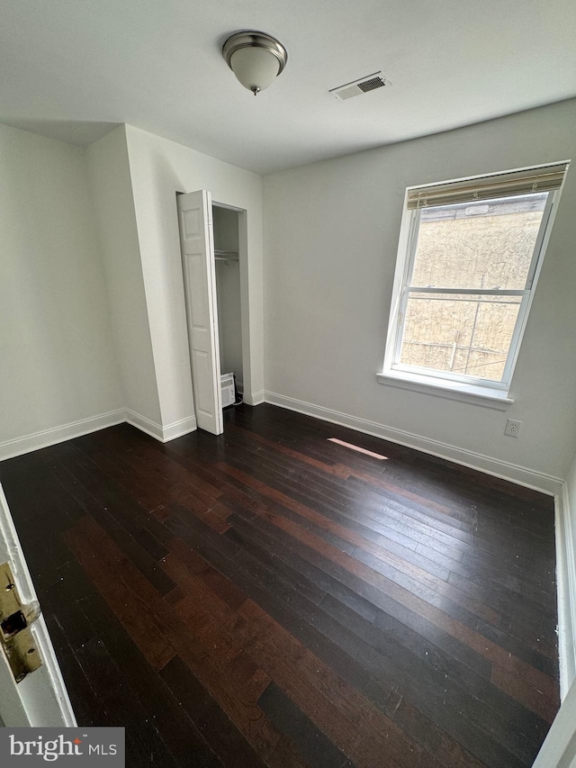 unfurnished bedroom featuring a closet, baseboards, visible vents, and dark wood-style flooring